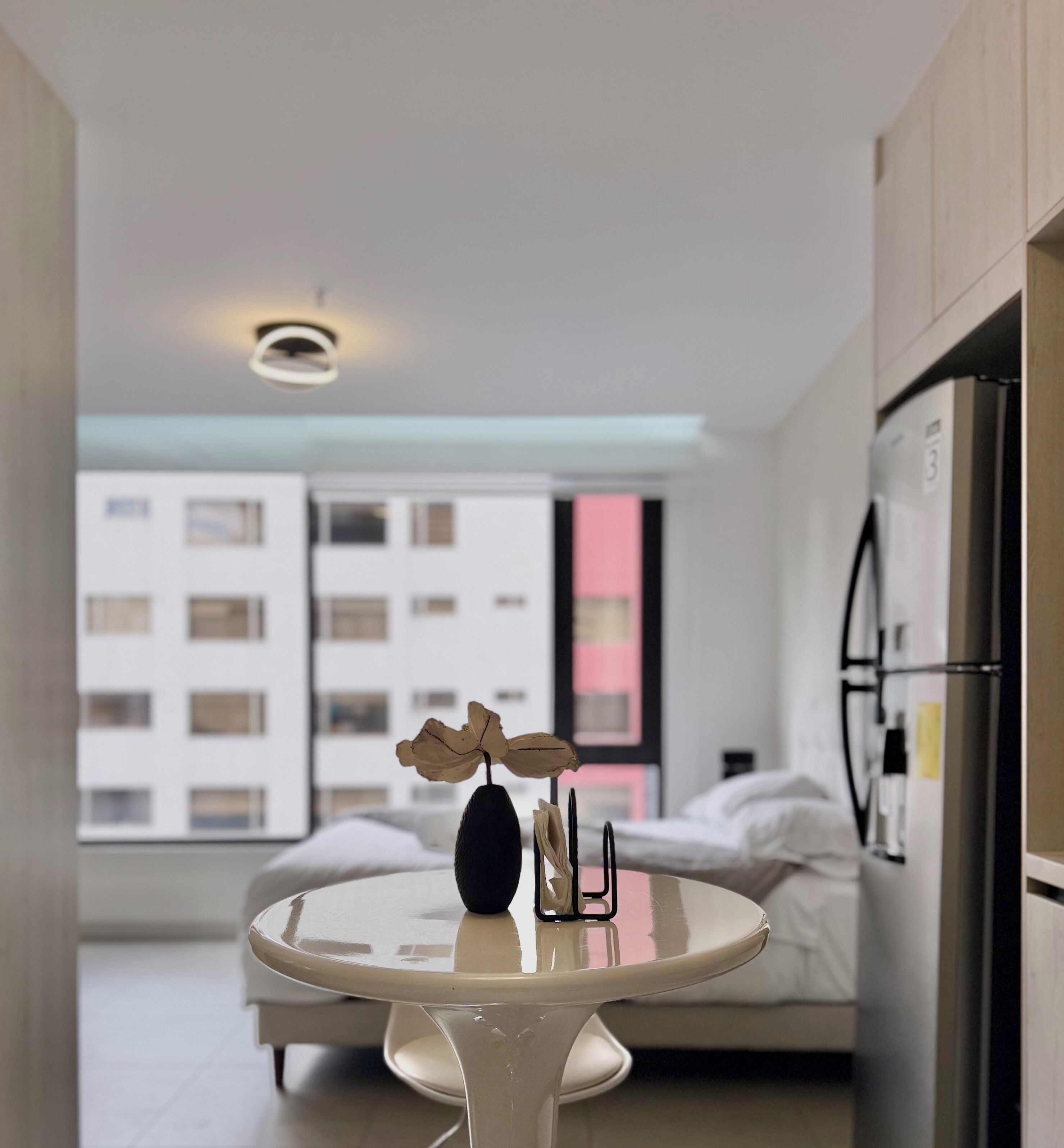 Eine moderne Küche mit einem runden Tisch, einem Kühlschrank und einem Fenster mit Blick auf ein Gebäude.