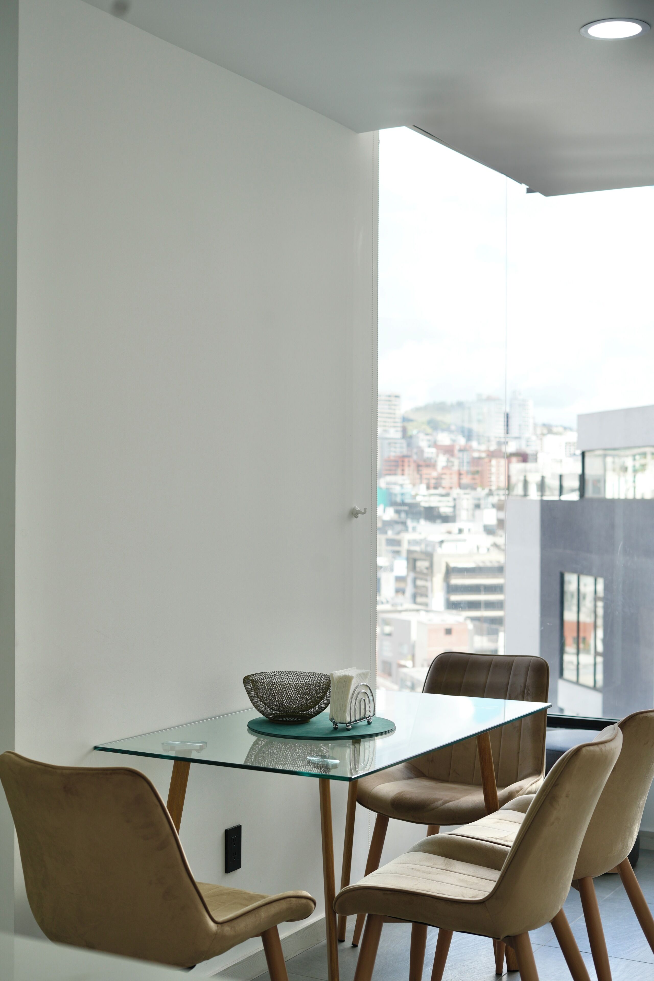 Un comedor moderno con una mesa de vidrio y dos sillas, un cuenco y una vela sobre la mesa.