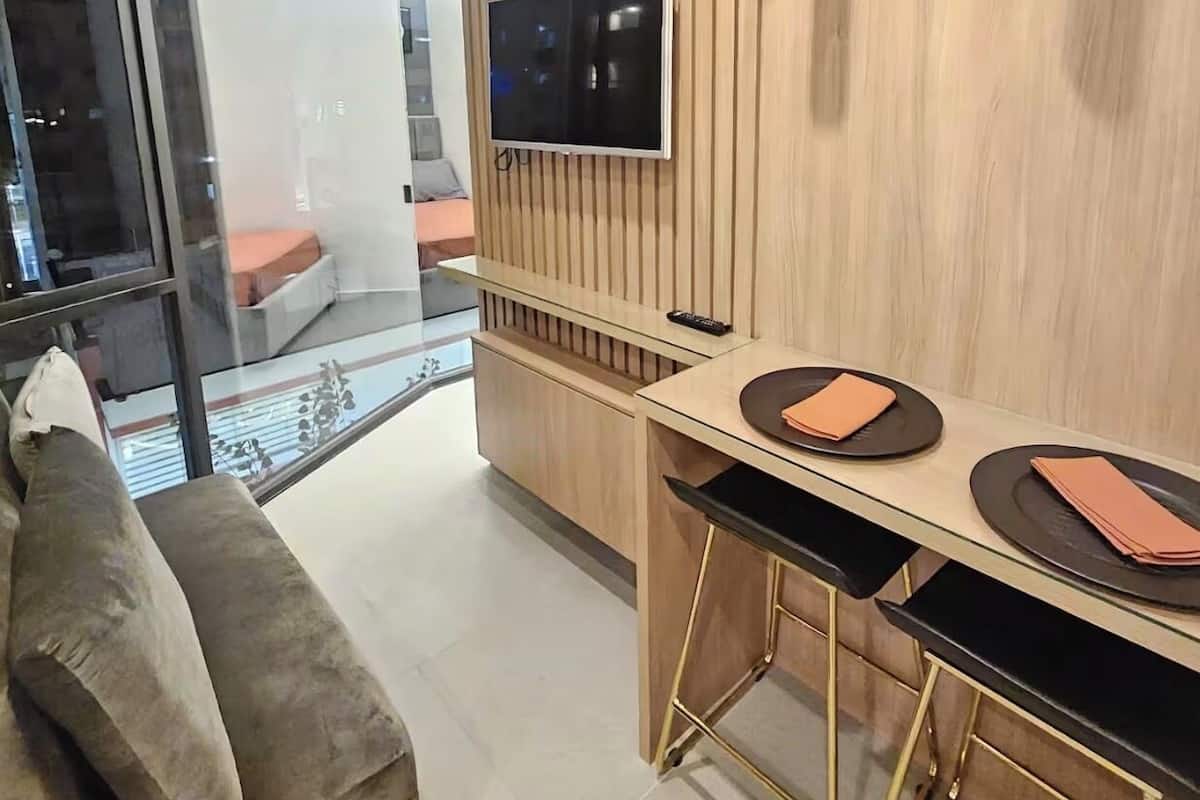 Una sala moderna con un panel de vidrio, un sofá, un comedor con mesa y sillas, un televisor montado y un panel de pared de madera.