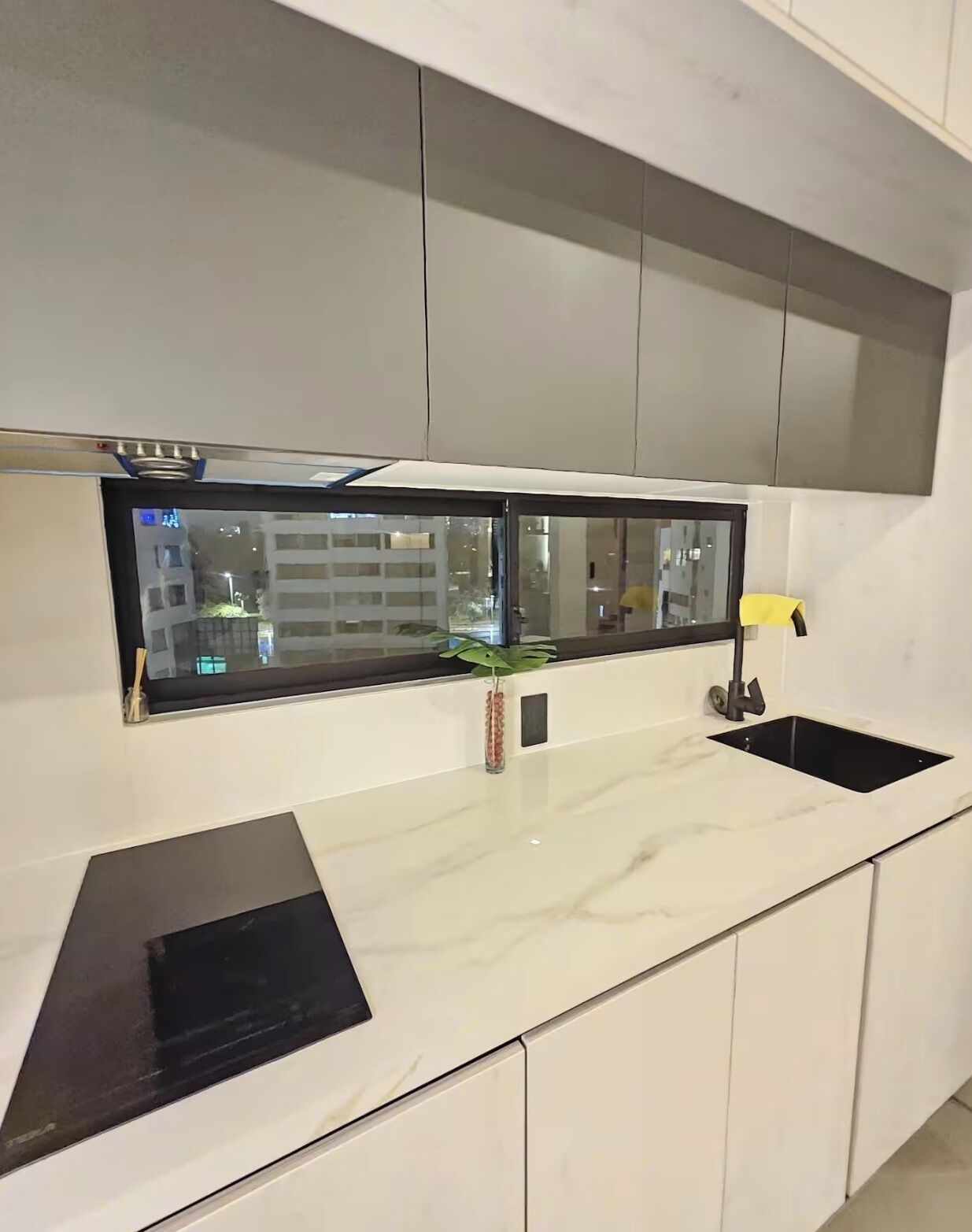 A modern kitchen with white cabinetry, black countertops, and a window with a view of buildings.