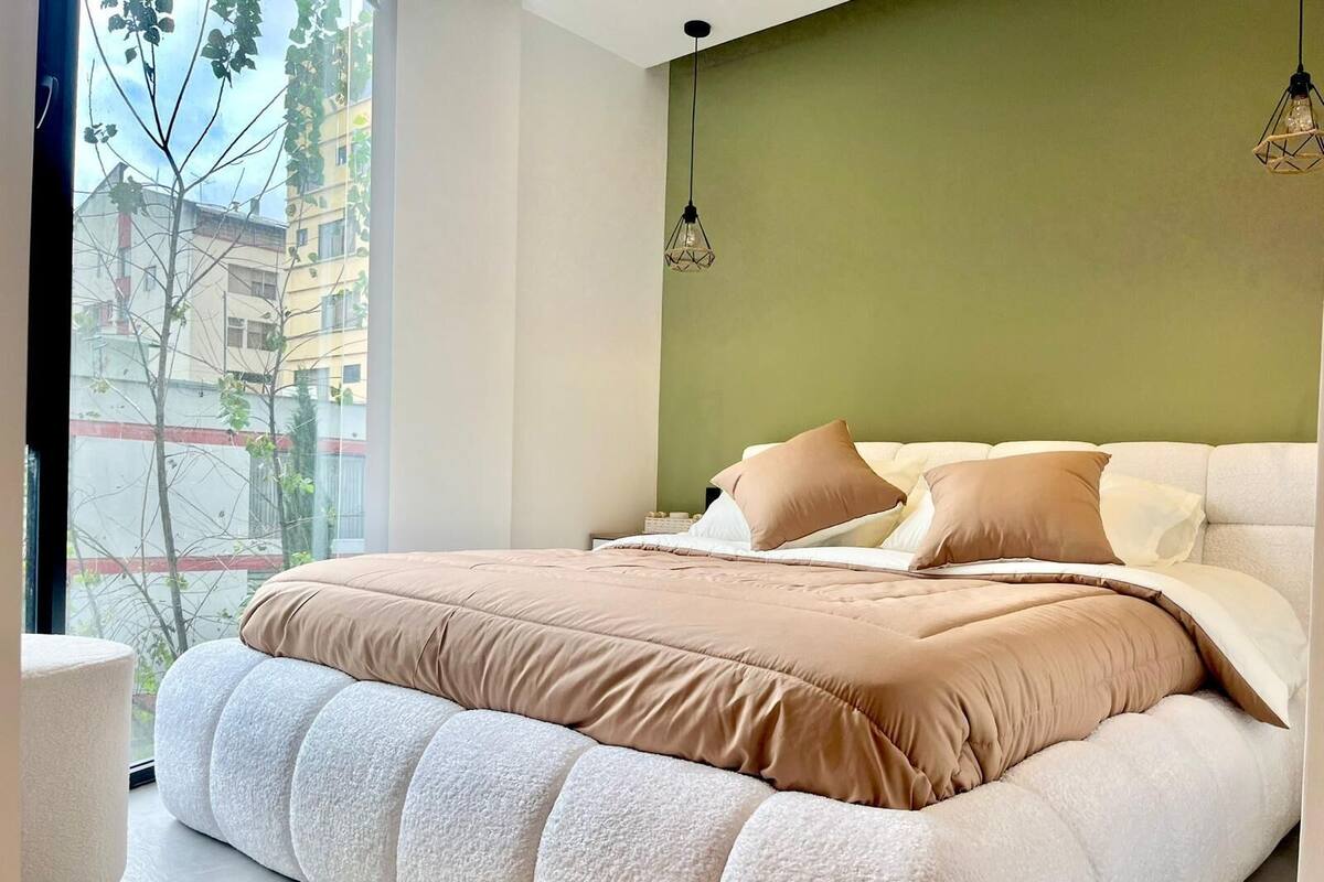 Un dormitorio moderno con una cama grande, paredes verdes y vistas a edificios.