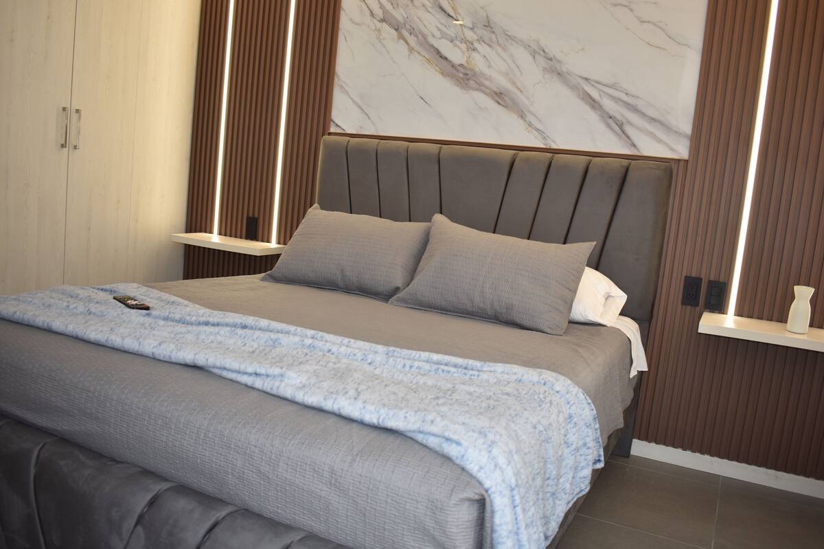 Un dormitorio moderno con una cama grande, cabecera con líneas verticales y pared con diseño de mármol.