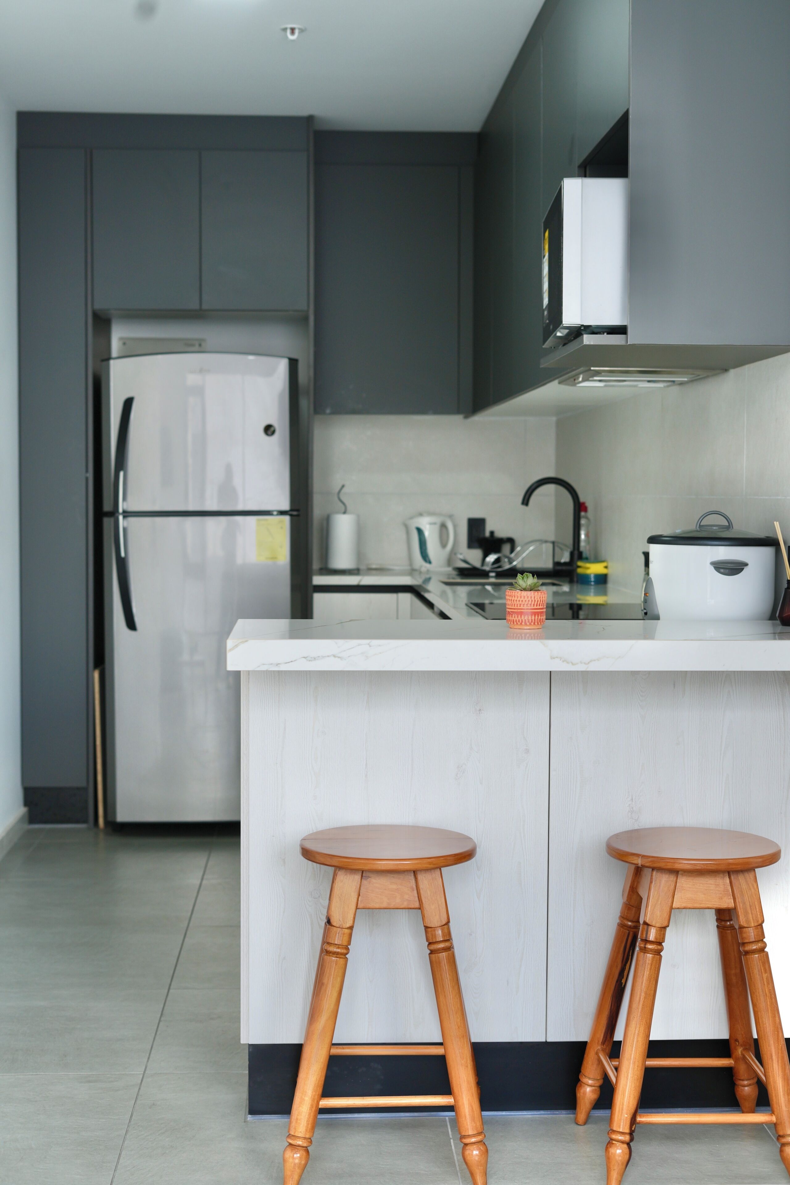 A modern kitchen with a stainless steel refrigerator, white cabinetry, a large island with stools, and a black faucet.