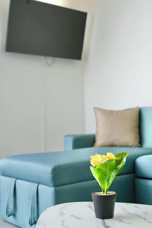 A living room with a teal sofa, a small potted plant on a white table, and a flat-screen TV mounted on the wall. - Harmony Luxury Apartments (Quito)