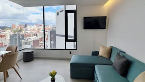 A modern living room with a large window, a sofa, a coffee table, and a flat-screen TV. - Harmony Luxury Apartments  (Quito)