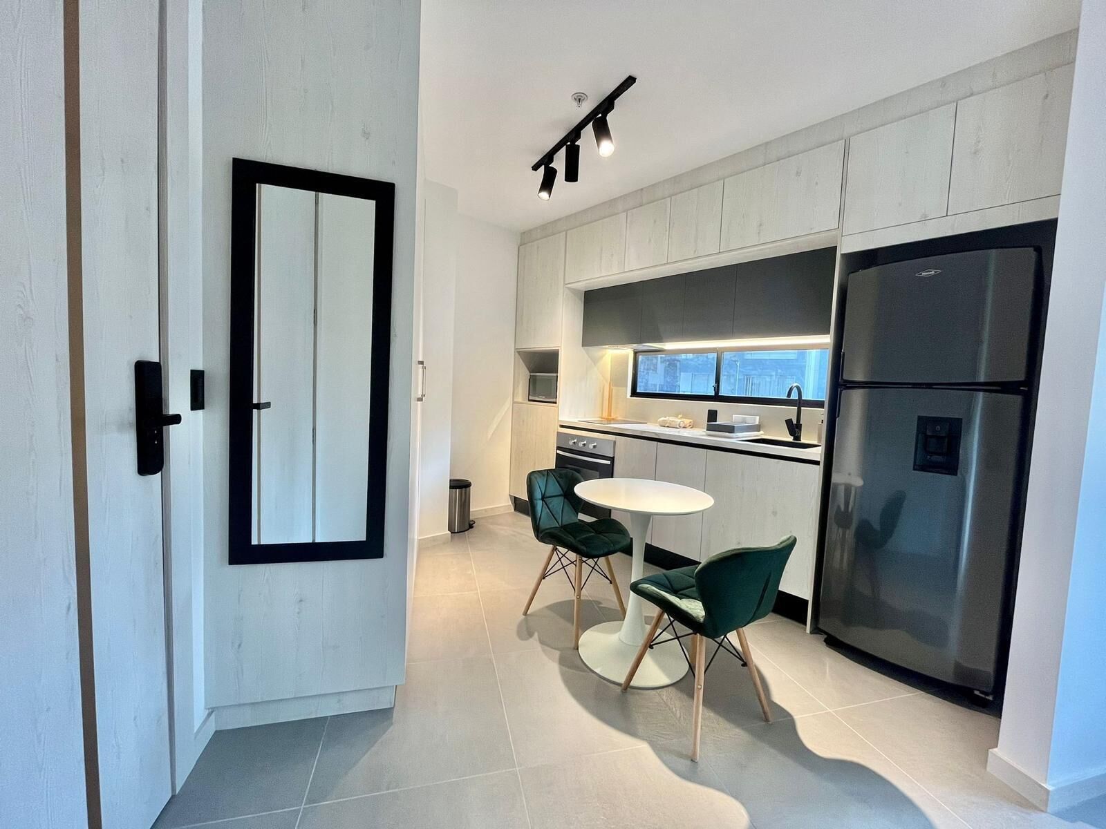 A modern kitchen with a dining area, featuring a large refrigerator, a sink, and a dining table with chairs.