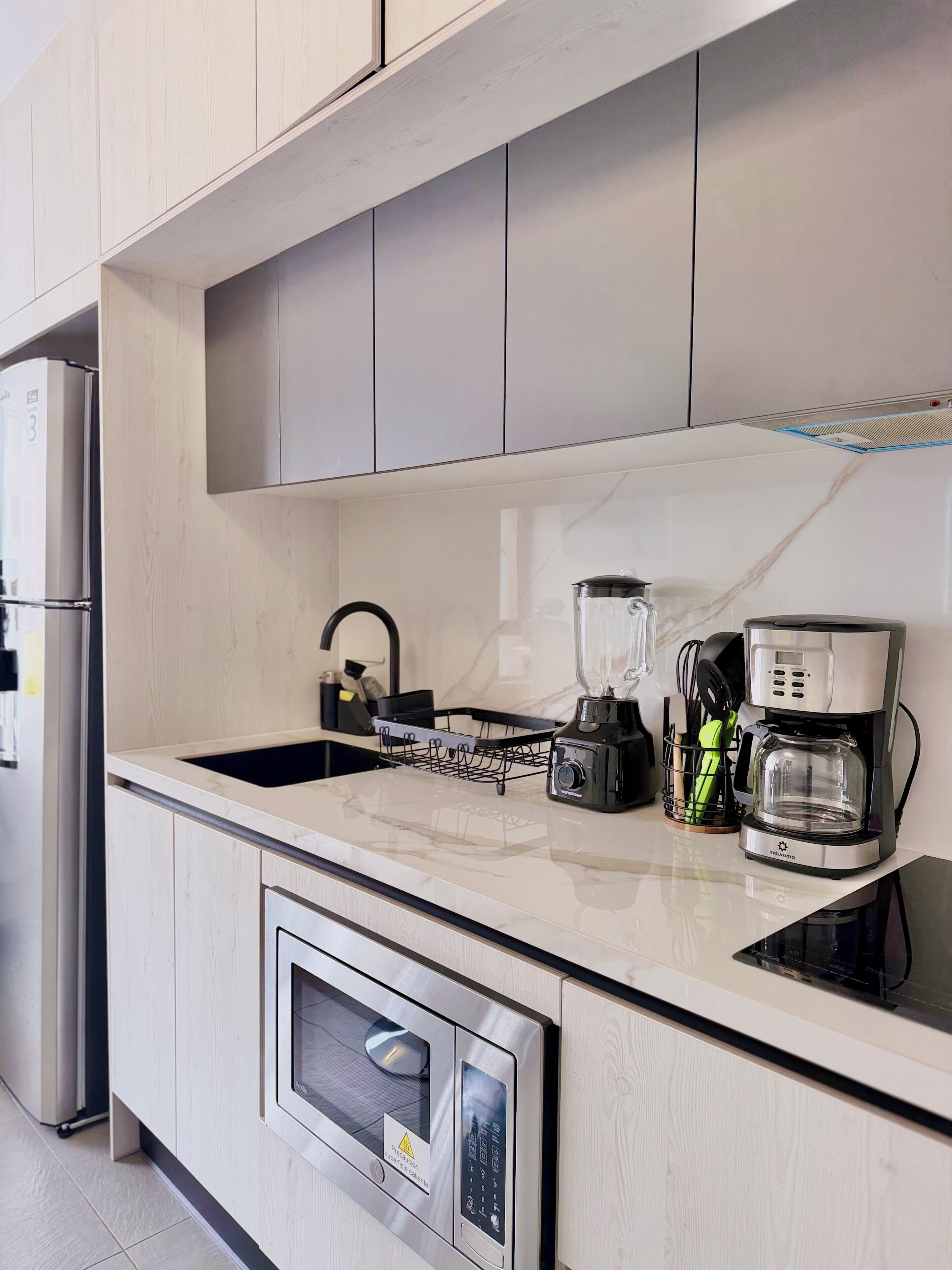 A modern kitchen with a built-in microwave, a coffee maker, and a kettle.
