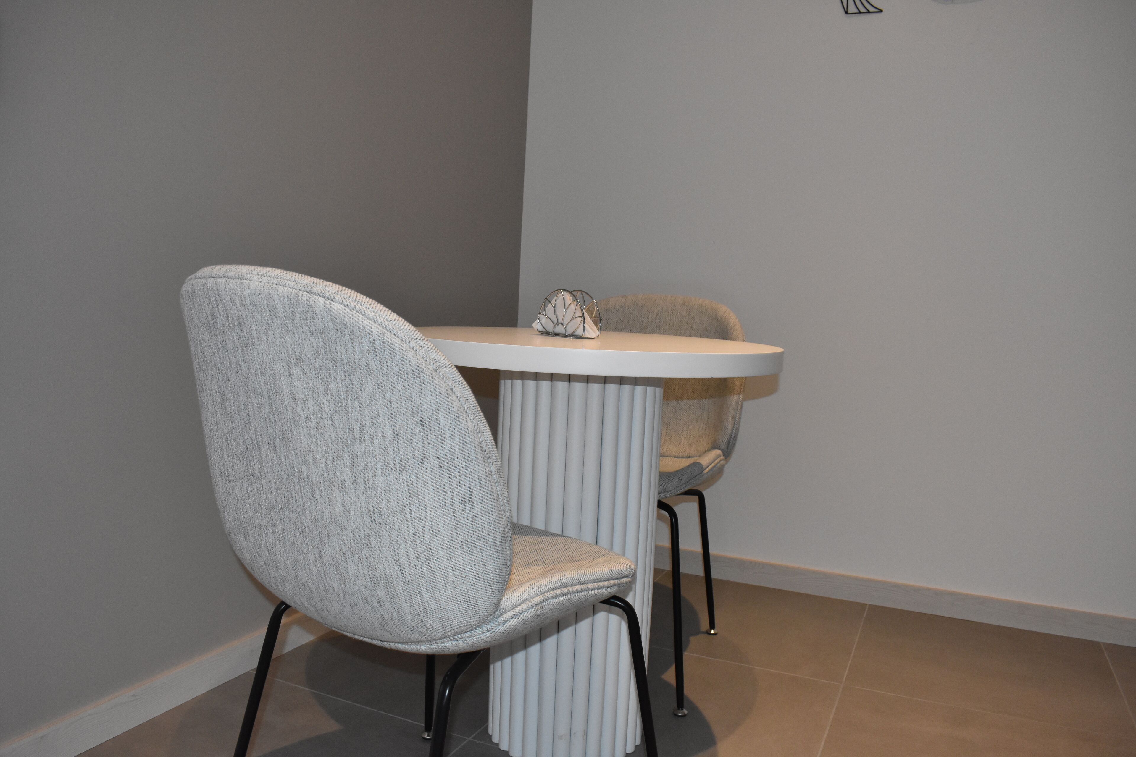 A modern dining area with a white table and two chairs, one with a textured fabric and the other with a smooth finish.