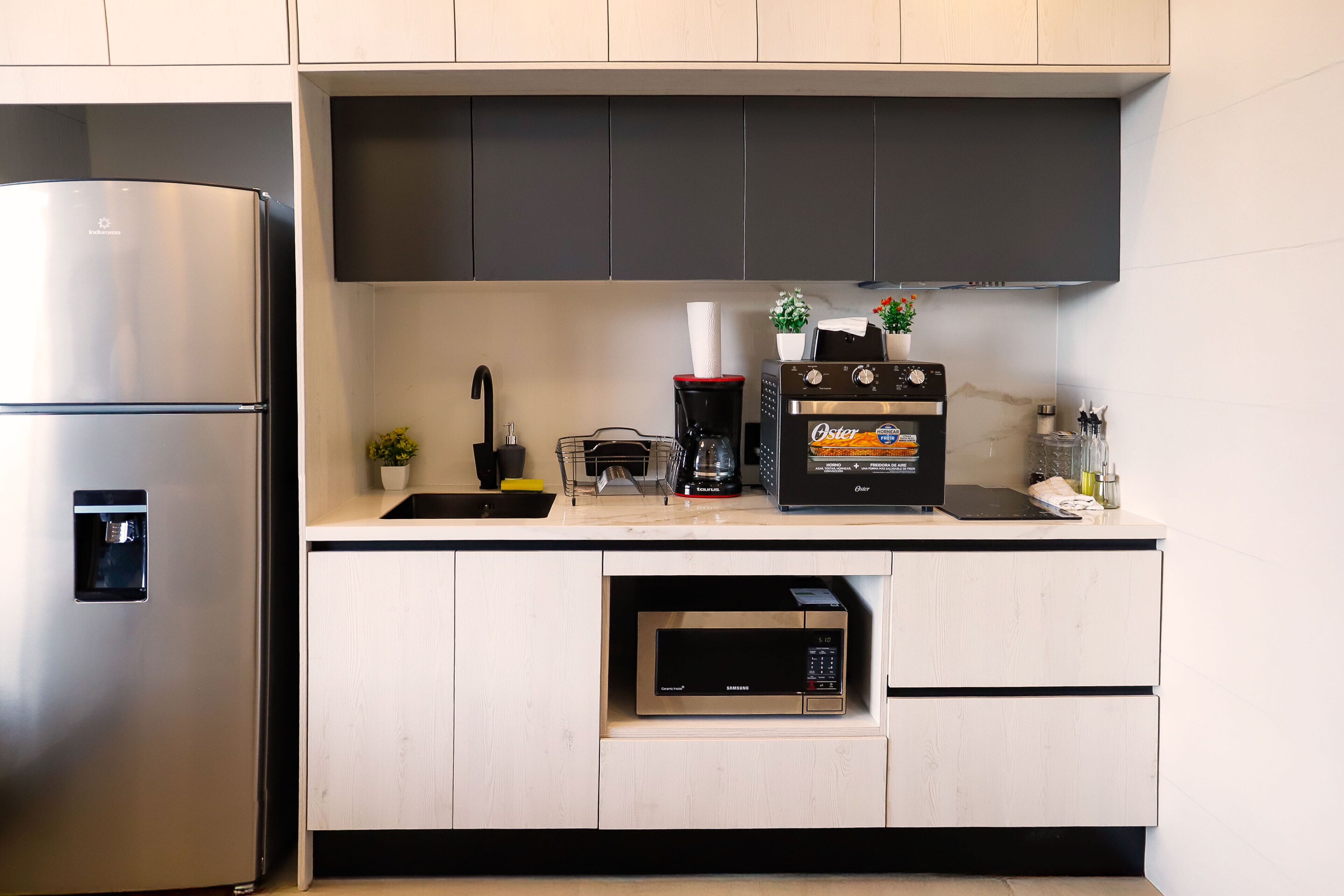 Une cuisine moderne équipée d’un réfrigérateur en acier inoxydable, d’un four à micro-ondes encastré et d’une machine à café posée sur le plan de travail.