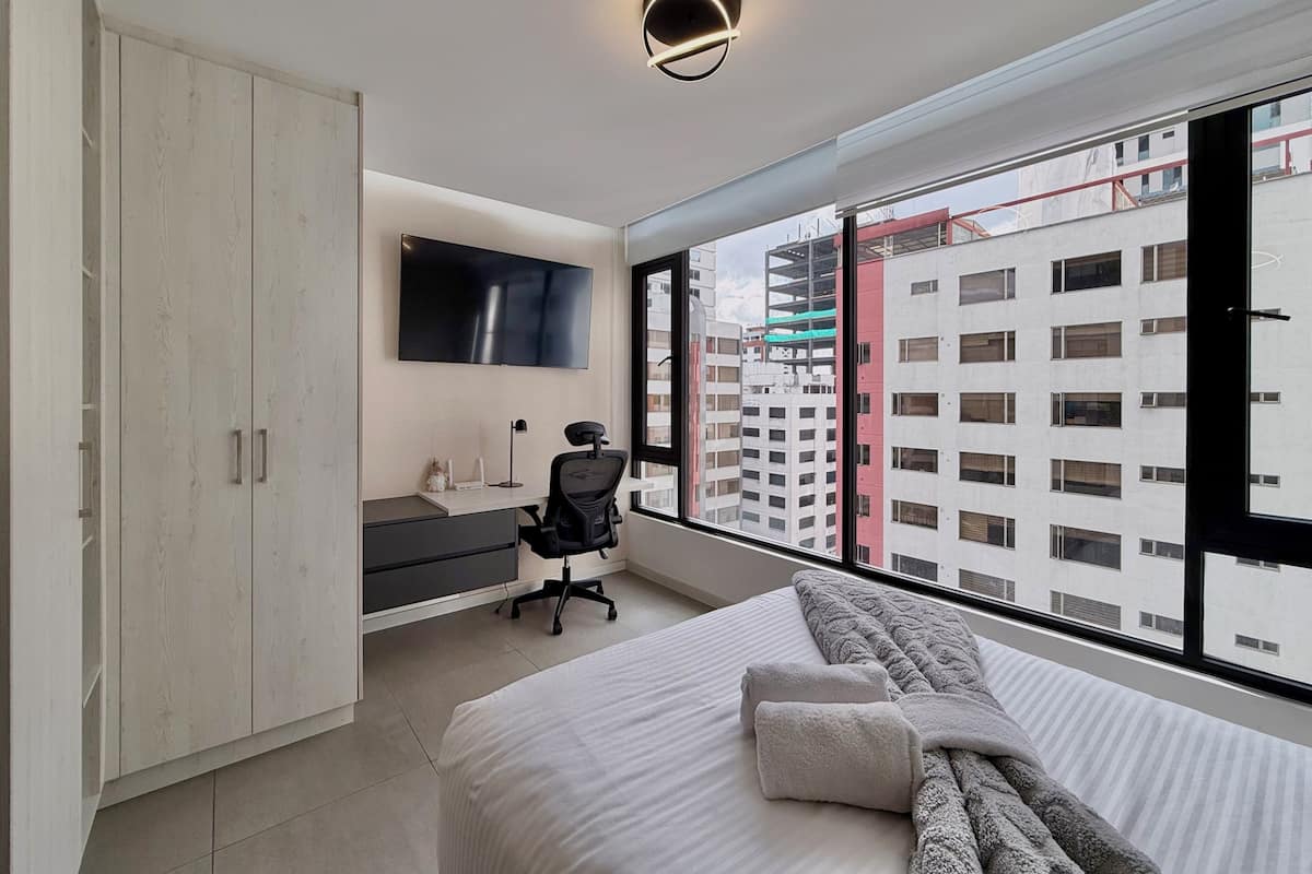 Un dormitorio moderno con cama, escritorio, silla, armario y televisor.