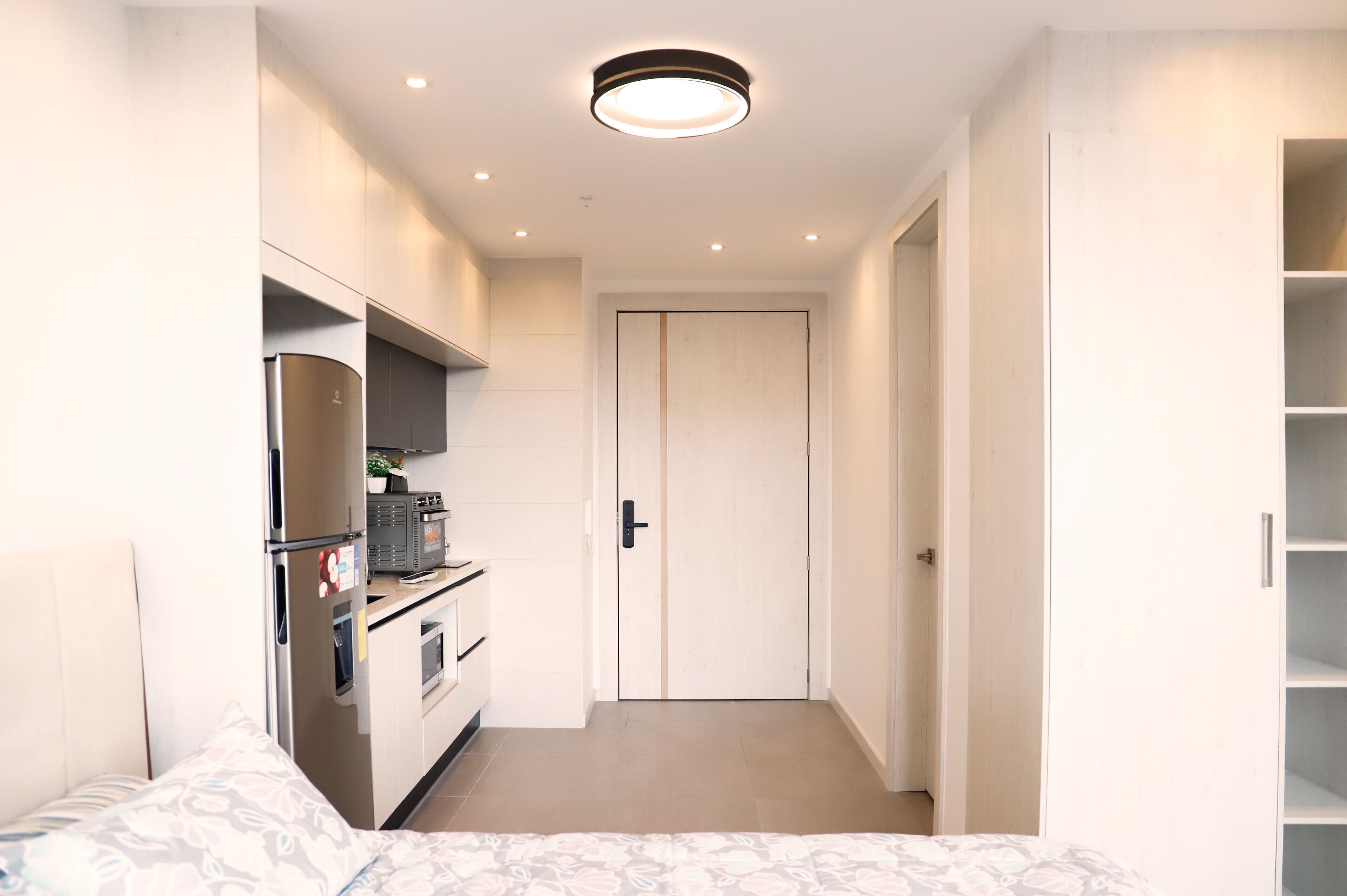 Une chambre d’hôtel de taille réduite comprenant un lit, une kitchenette, une armoire et une porte donnant sur une autre pièce.