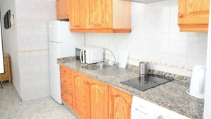 A compact kitchen with wooden cabinets, a built-in oven, a microwave, a sink, and a dishwasher. - Apt. ManRey 2A - Turquesa (Valle Gran Rey)