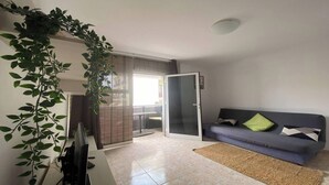 A living room with a sofa, a desk with a computer, and a plant. - Apt. ManRey 1B - Ambar (Valle Gran Rey)