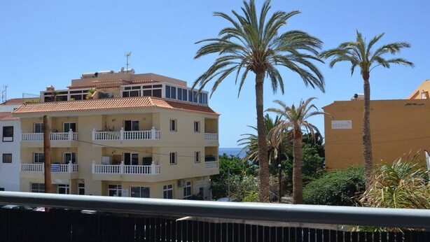 A multi-story building with balconies, a tiled roof, and a sign indicating a beach location. - Apt. ManRey 1B - Ambar (Valle Gran Rey)
