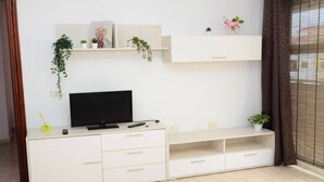 A white entertainment unit with a flat-screen TV, remote controls, and decorative items. - Apt. ManRey 1B - Ambar (Valle Gran Rey)