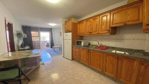 A kitchen with wooden cabinets, a refrigerator, a microwave, and a sink. - Apt. ManRey 1B - Ambar (Valle Gran Rey)