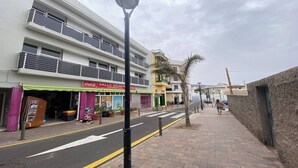 A street view with a multi-story building featuring a 'Coca-Cola' sign and a 'Valle Gran R' supermarket. - Apt. ManRey 1B - Ambar (Valle Gran Rey)