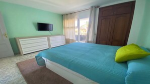 A bedroom with a bed, a television on the wall, a wardrobe, and a window with curtains.