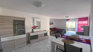 A modern living room with a dining area, a glass cabinet, a mirror, and a balcony with a pink curtain.