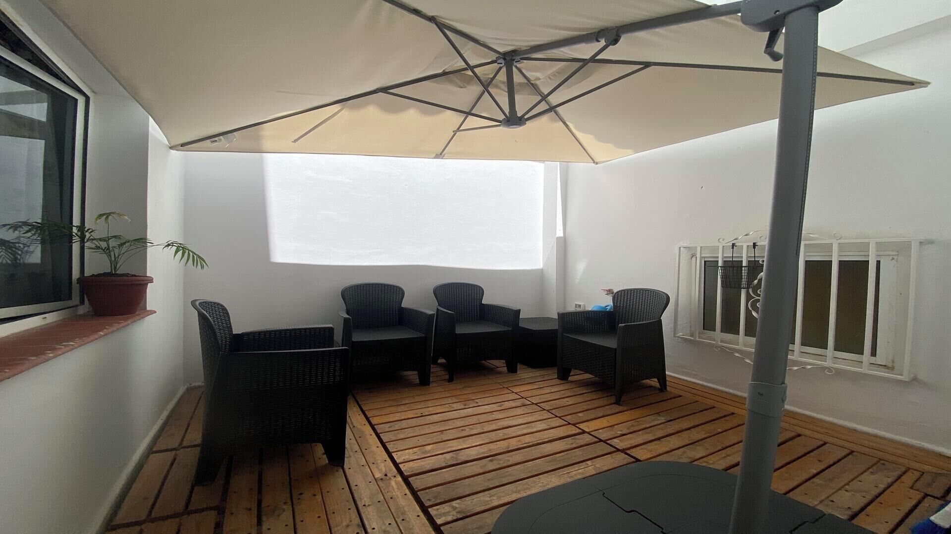 Een terras met rieten meubilair, een grote parasol en een potplant.