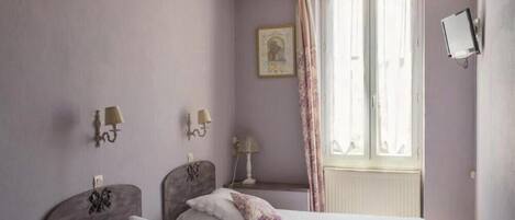Una habitación con dos camas, una ventana con cortinas, un televisor montado en la pared y apliques en la pared.