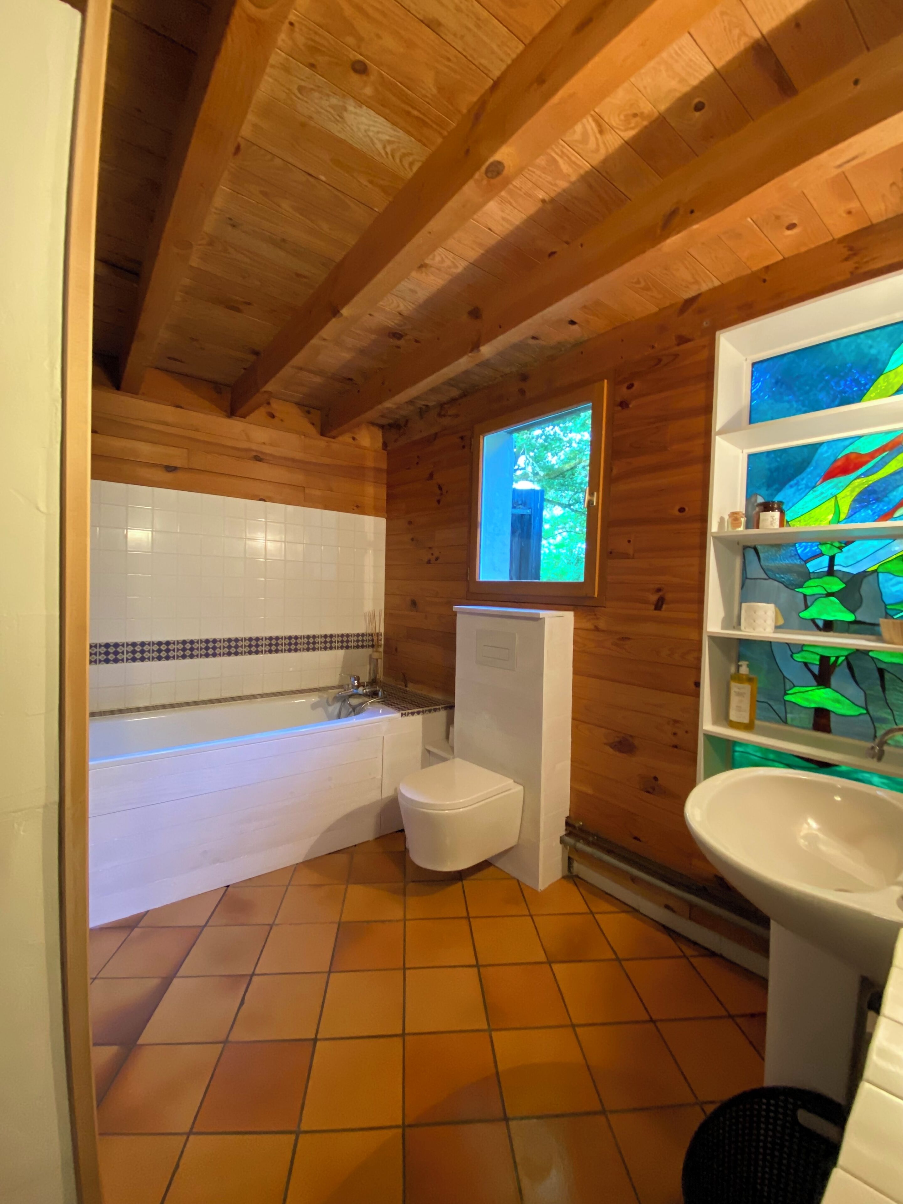 A wooden cabin bathroom with a white toilet, a bathtub, and a sink.
