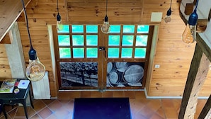 Een houten interieur met een groot raam, meerdere lampen en een deur met uitzicht op vaten.