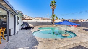 Una piscina dalla forma sinuosa, circondata da un patio con sedie e un ombrellone.