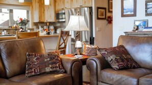 A cozy living room with leather sofas, patterned throw pillows, a wooden coffee table, and a lamp.