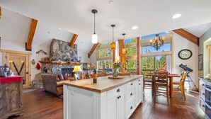 A spacious kitchen with a large island, wooden beams, and a stone fireplace.