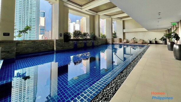 Una amplia piscina interior con baldosas azules y cristalinas, rodeada de muros de piedra y plantas en macetas.