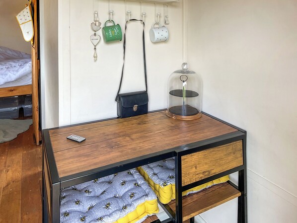 Un lit en bois avec une tête de lit, une table de chevet avec une télécommande, un petit sac noir et un objet décoratif accroché au mur.