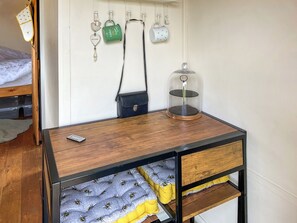 Un lit en bois avec une tête de lit, une table de chevet avec une télécommande, un petit sac noir et un objet décoratif accroché au mur.