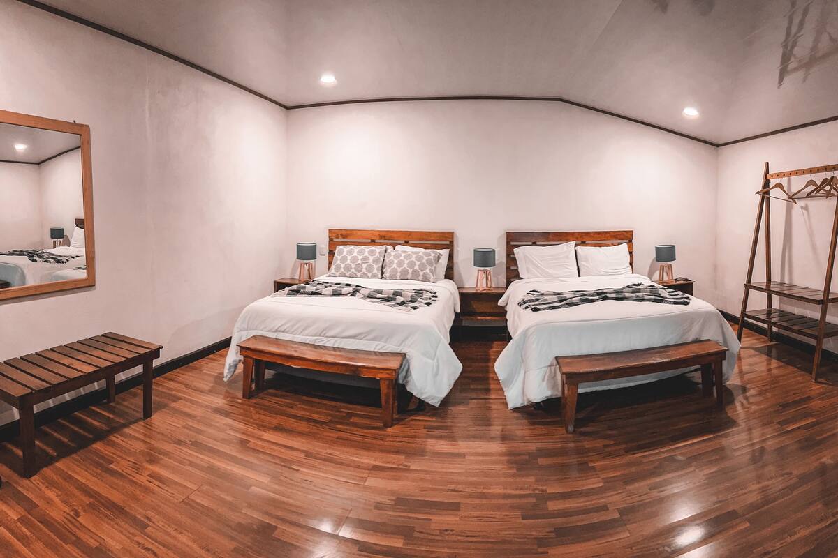 Ein Schlafzimmer mit zwei Betten, Holzbanken, einem Spiegel und einem Kleiderständer.