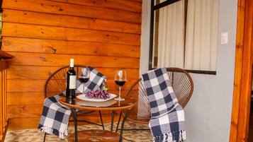 Un interior de madera con una mesa dispuesta para dos personas, que incluye una botella de vino, una copa y un plato de uvas.