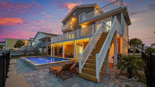 A two-story house with a swimming pool, outdoor seating, and a staircase leading to the upper level. - 4 BR Waterview Home- Pool- Gameroom- Sleeps 11 (North Myrtle Beach)