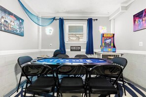 A room with a blackjack table, chairs, a neon sign, and a neon sign indicating a game zone.