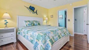 Ein Schlafzimmer mit einem Bett, zwei Nachttischen, einem Deckenventilator und einer Tür zu einem anderen Raum.