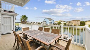 A wooden deck with a table and chairs, overlooking a body of water and a row of houses. - 4 BR Waterview Home- Pool- Gameroom- Sleeps 11 (North Myrtle Beach)