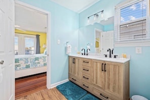 Une salle de bain avec un meuble-lavabo en bois, deux vasques et une fenêtre avec des stores.