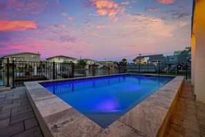 A rectangular swimming pool with a black metal fence and a stone border, surrounded by a paved deck.