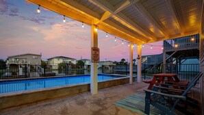 A swimming pool area with a covered deck, a lifeguard warning sign, and a view of residential buildings in the background. - 4 BR Waterview Home- Pool- Gameroom- Sleeps 11 (North Myrtle Beach)
