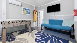 Ein Zimmer mit einer Fußballstoßmaschine, einem blauen Sofa, einem Fernseher und einem Feuerlöscher.