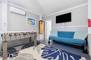 Ein Zimmer mit einer Fußballstoßmaschine, einem blauen Sofa, einem Fernseher und einem Feuerlöscher.