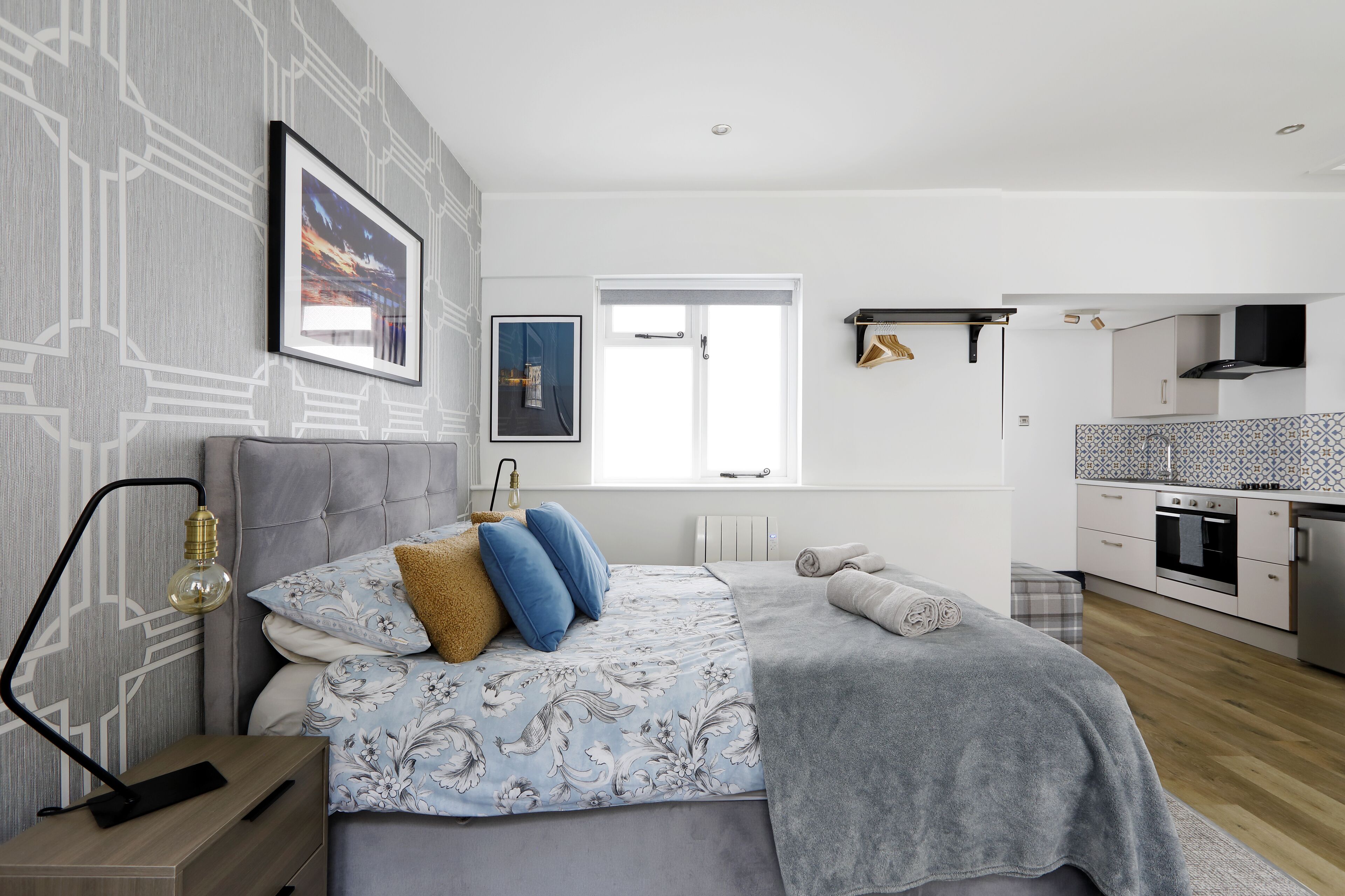 A modern bedroom with a bed, bedside table, lamp, and a view of the kitchen.