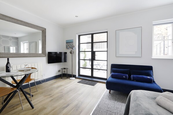 A modern living room with a sofa, a dining table with chairs, a large mirror, and a TV. - Brighton Courtyard boutique (Brighton)