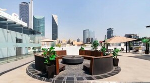 Relax in a serene rooftop setting with a circular seating area surrounded by lush greenery and a stunning city view.