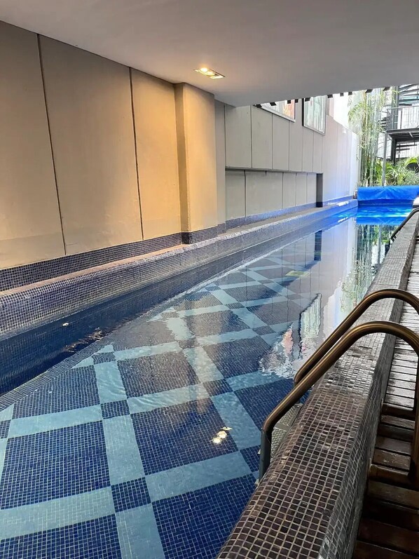 Swimmers can enjoy the pool surrounded by a wooden deck with metal handrails.