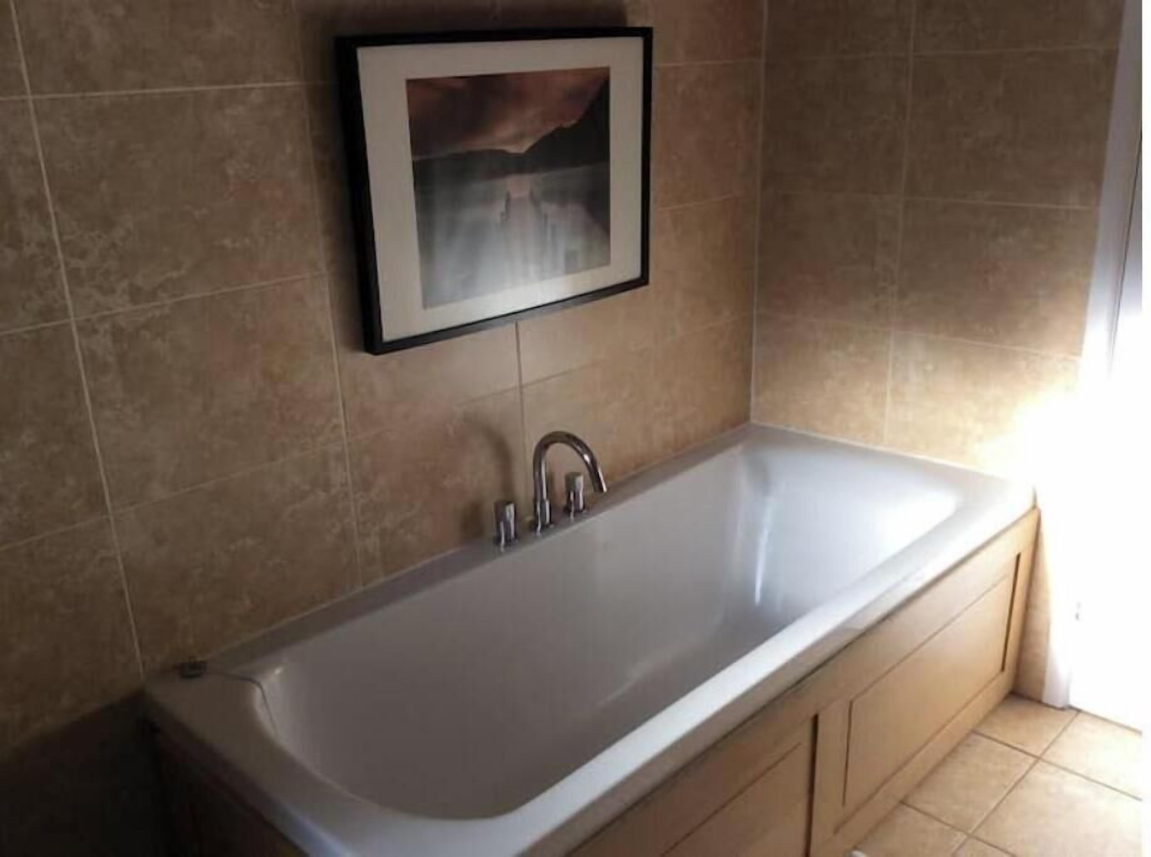 Une salle de bain avec une grande baignoire, des murs recouverts de carreaux beiges et un tableau encadré au-dessus du lavabo.