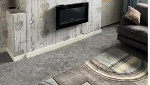A living room with a flat-screen TV mounted above a fireplace, a sofa, and patterned wallpaper.